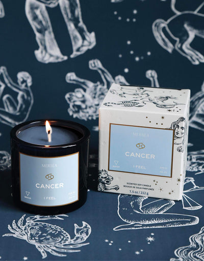 Mersea Cancer scented candle displayed beside its accompanying box, set against an astrology sign-themed backdrop