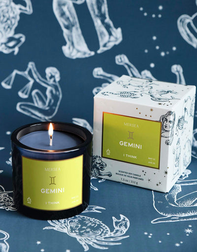 Mersea Gemini scented candle displayed beside its accompanying box, set against an astrology sign-themed backdrop