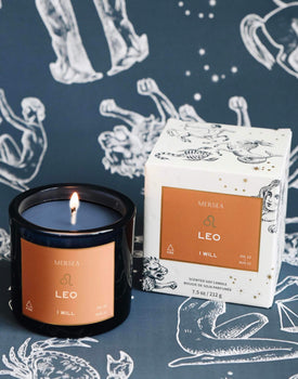 Mersea Leo scented candle displayed beside its accompanying box, set against an astrology sign-themed backdrop