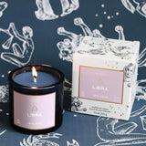 Mersea Libra scented candle displayed beside its accompanying box, set against an astrology sign-themed backdrop