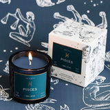 Mersea Pisces scented candle displayed beside its accompanying box, set against an astrology sign-themed backdrop