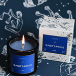 Mersea Sagittarius scented candle displayed beside its accompanying box, set against an astrology sign-themed backdrop