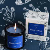 Mersea Sagittarius scented candle displayed beside its accompanying box, set against an astrology sign-themed backdrop