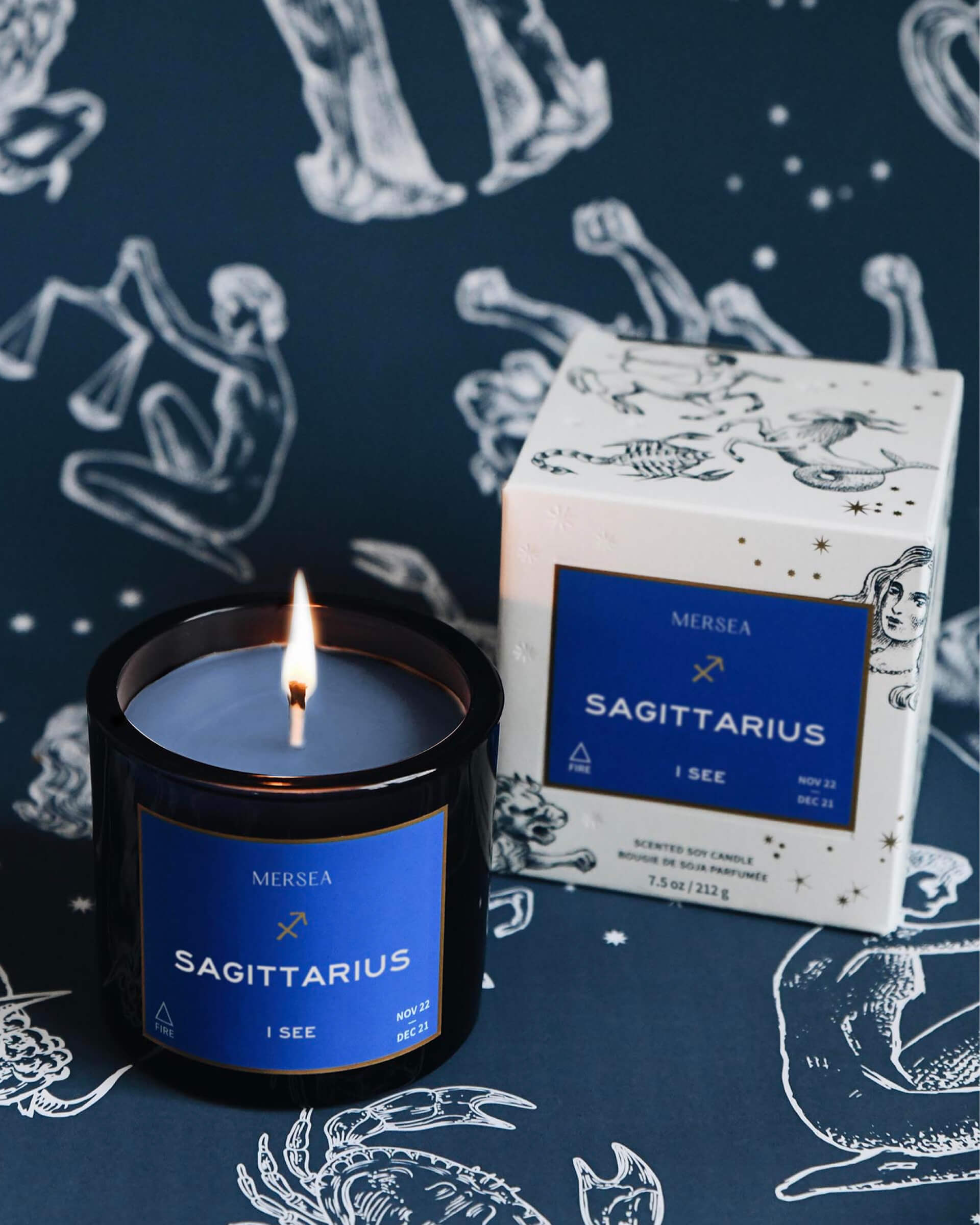 Mersea Sagittarius scented candle displayed beside its accompanying box, set against an astrology sign-themed backdrop