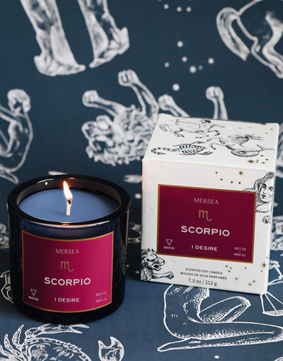 Mersea Scorpio scented candle displayed beside its accompanying box, set against an astrology sign-themed backdrop