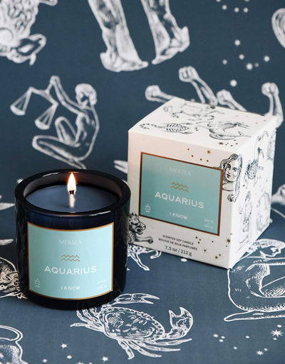Mersea Aquarius scented candle displayed beside its accompanying box, set against an astrology sign-themed backdrop