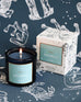 Mersea Aquarius scented candle displayed beside its accompanying box, set against an astrology sign-themed backdrop