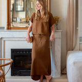 Woman in a brown outfit standing in a room with a fireplace and mirror.