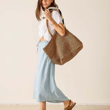 Woman holding a woven bag against a plain background