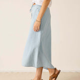 Person wearing a light blue skirt and brown sandals on a plain background