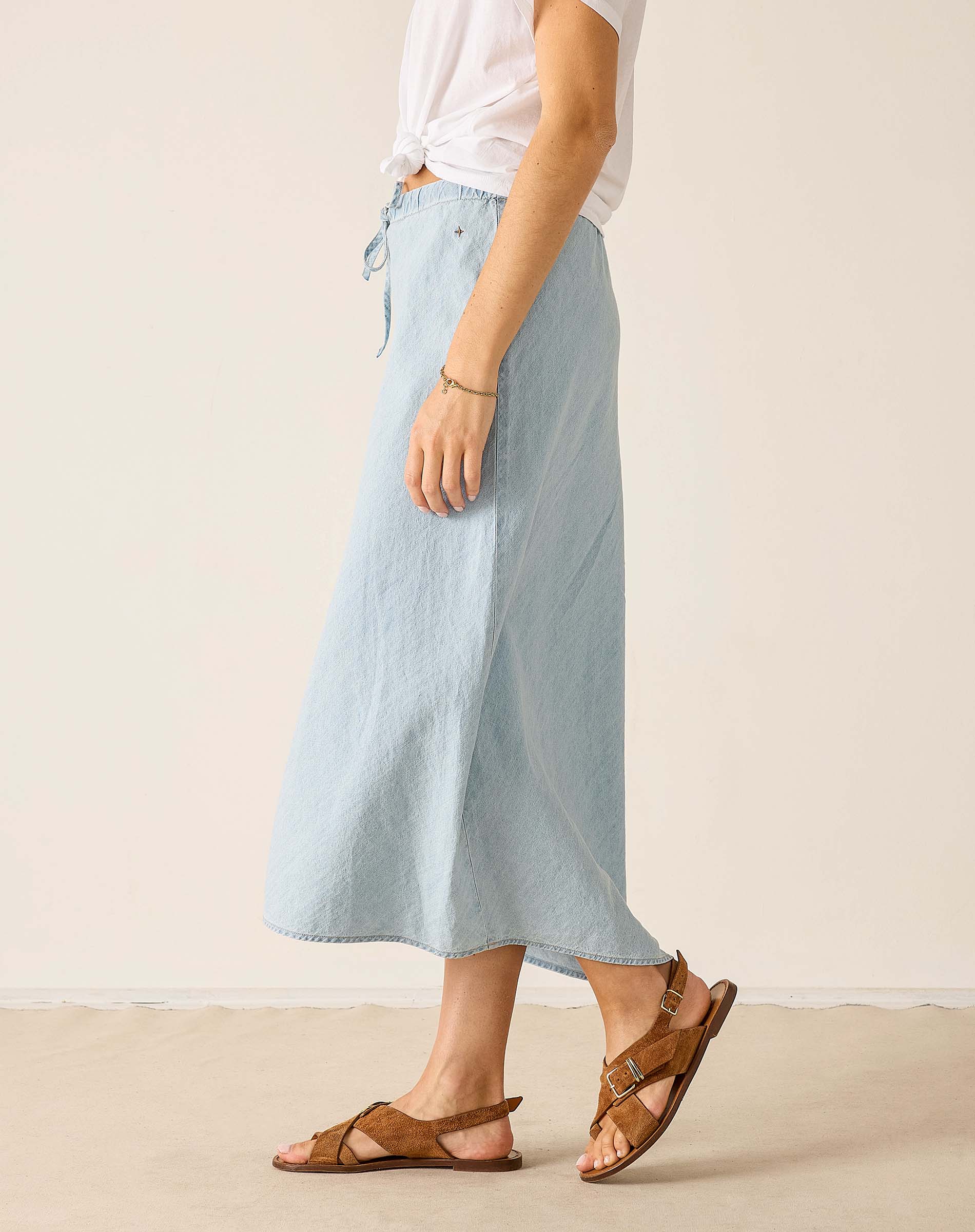 Person wearing a light blue skirt and brown sandals on a plain background