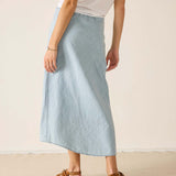 Person wearing a light blue skirt and white top on a plain background
