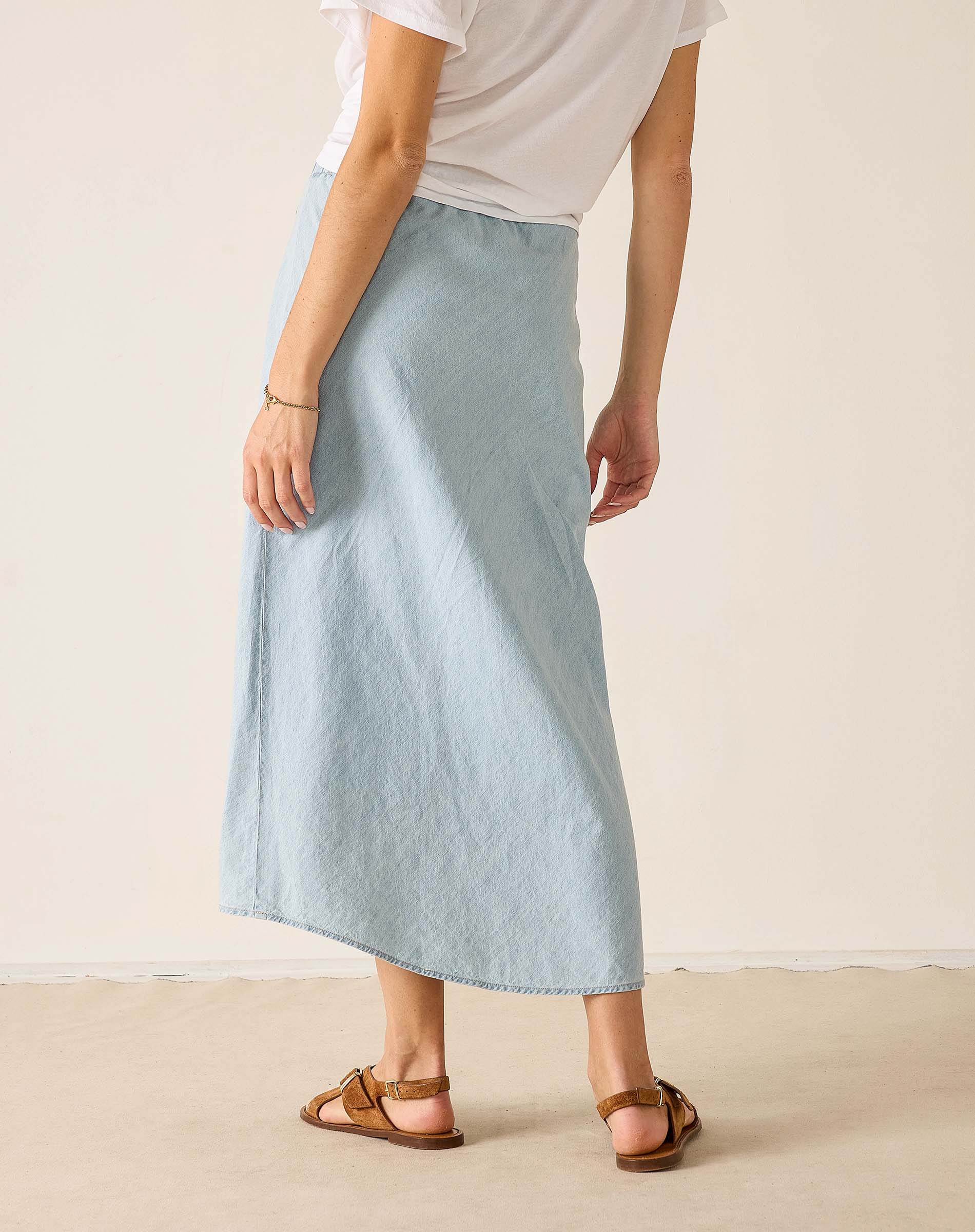 Person wearing a light blue skirt and white top on a plain background