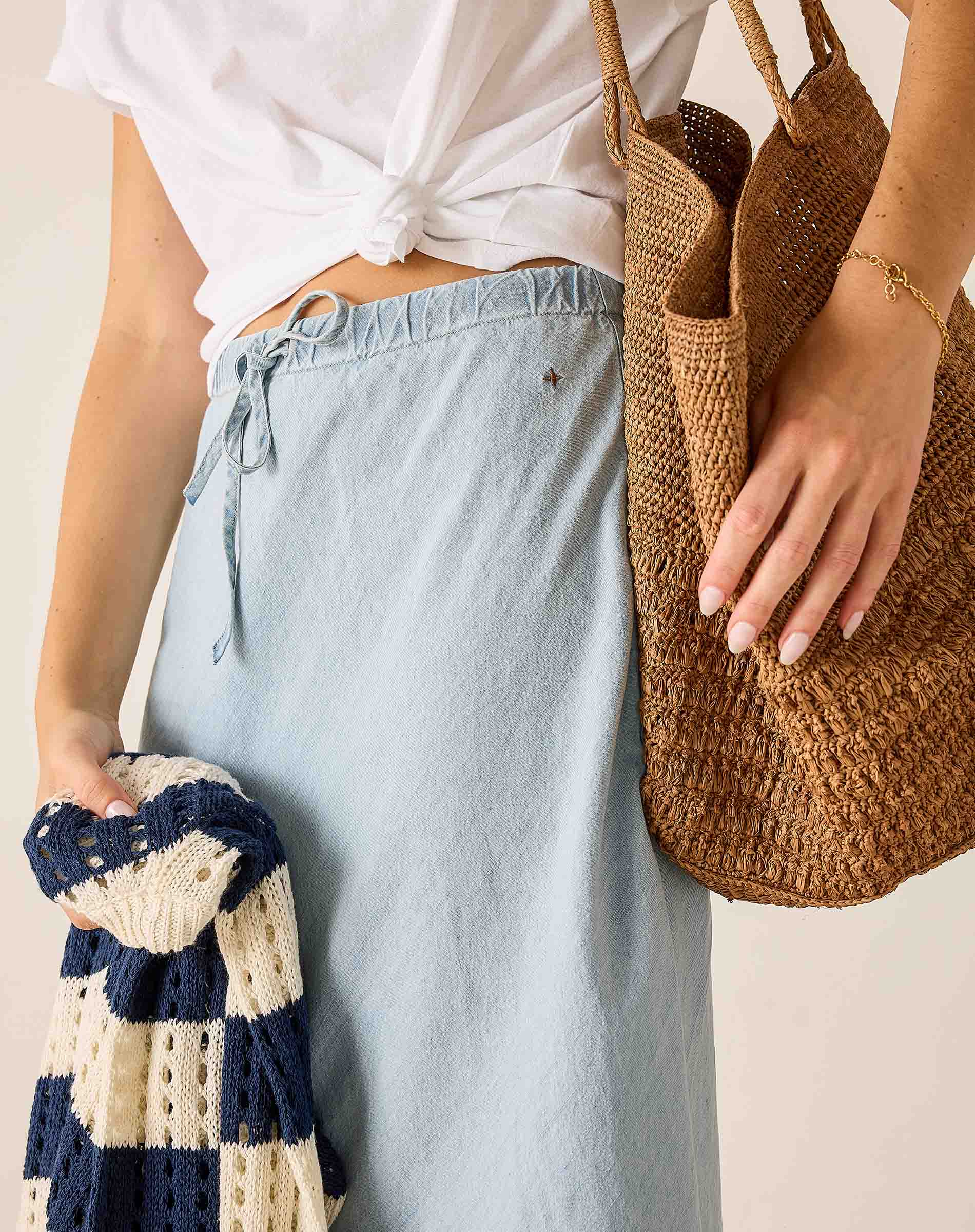 Person holding a woven bag and a knitted item against a neutral background