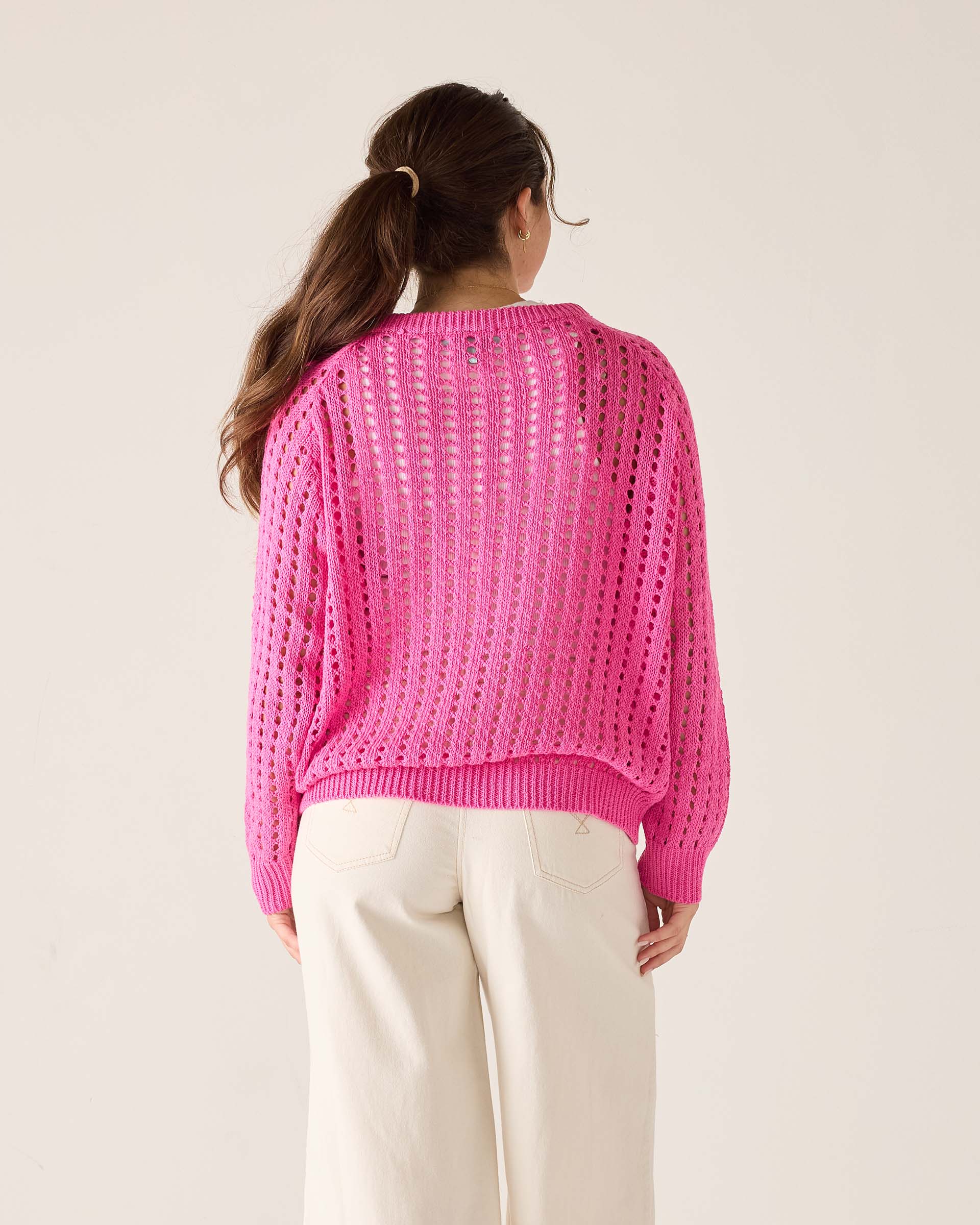 Person wearing a bright pink knitted sweater on a plain background