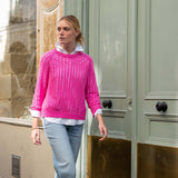 Woman wearing a pink sweater and light blue jeans standing in front of a building entrance.