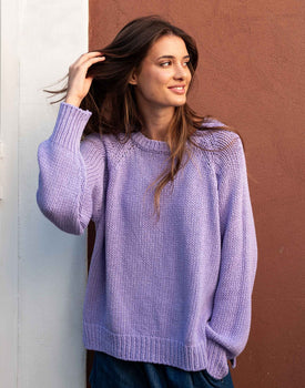 Female wearing a purple knit sweater in front of orange wall