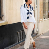 Woman wearing a blue and white striped scarf, white shirt, beige pants, and brown sandals on a city street.