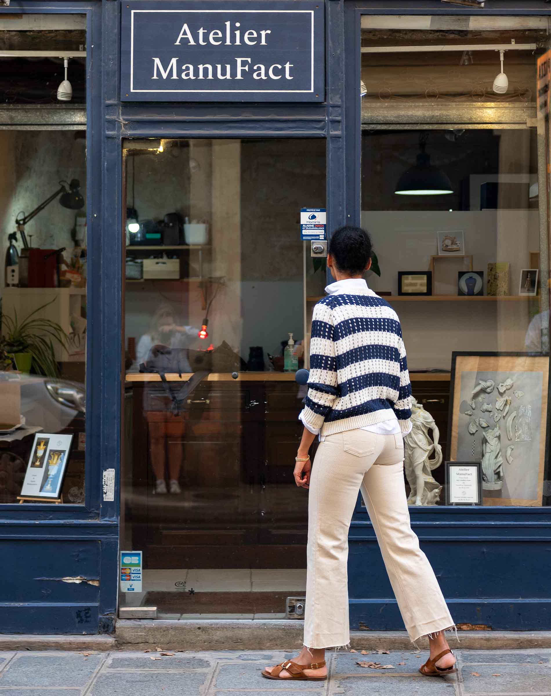 Person walking past a store named 'Atelier ManuFact' with art displayed inside.