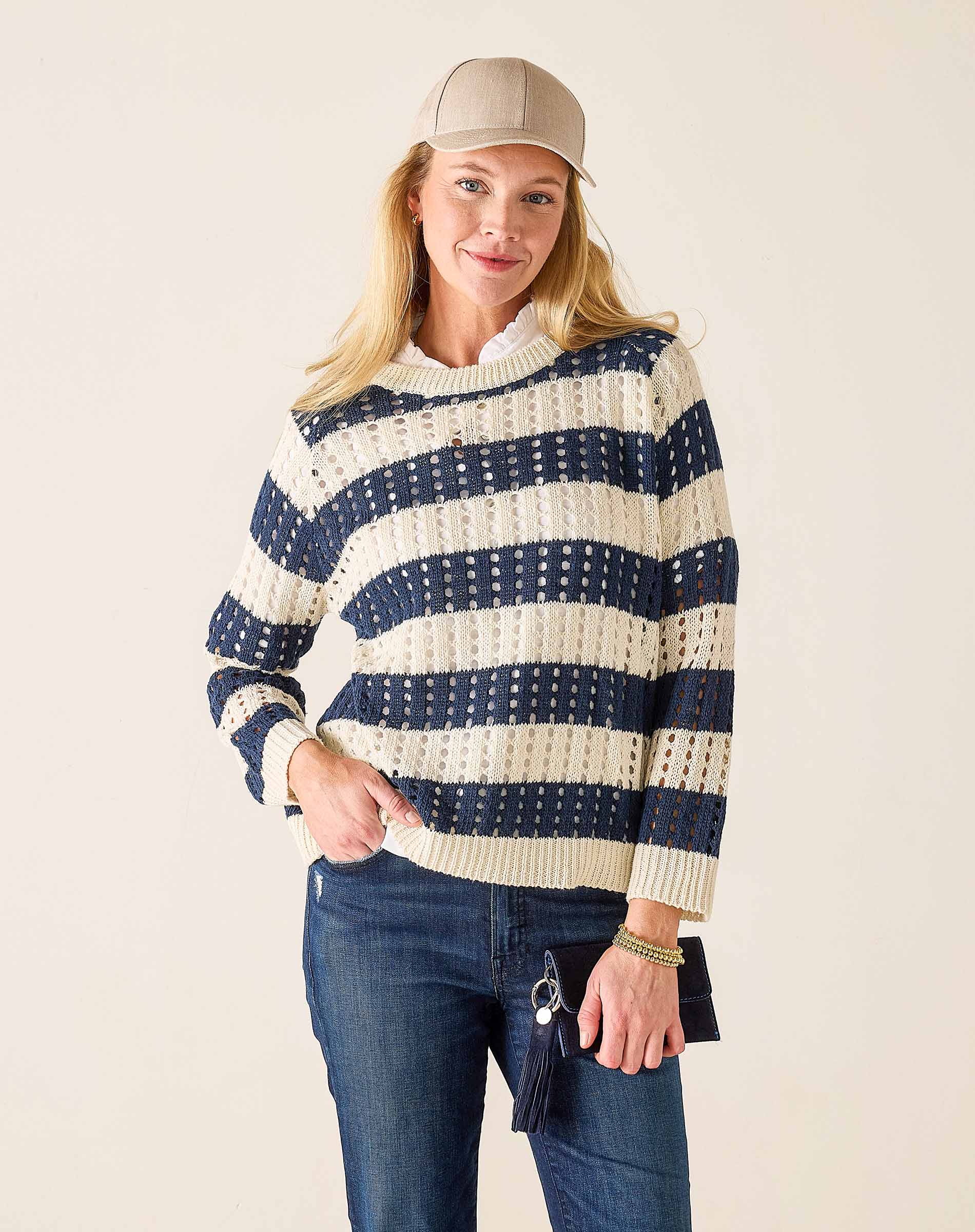 Woman wearing a navy and white striped sweater with blue jeans on a beige background