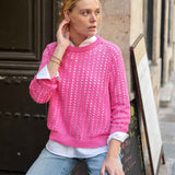 Woman wearing a pink knitted sweater and light blue jeans sitting on a step.