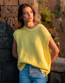 Female wearing a yellow knit vest in stand with her hand in her back at sunset
