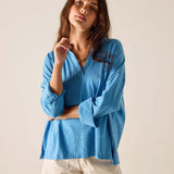 Woman wearing a blue shirt and white shorts against a plain background