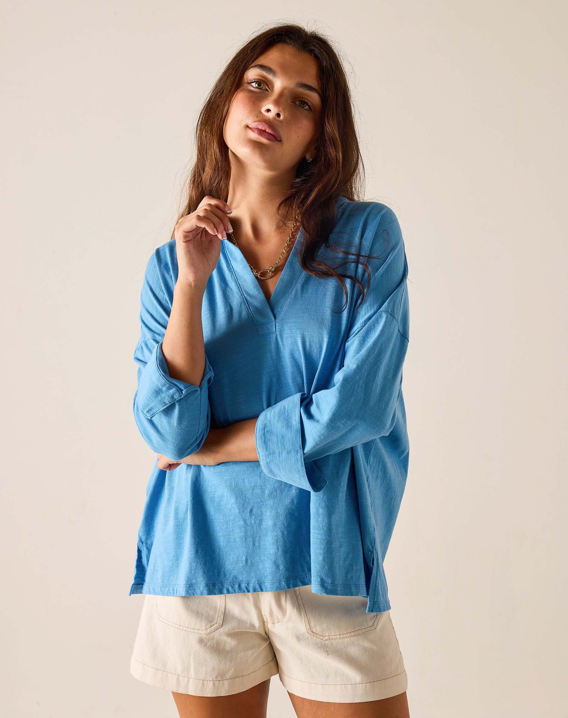 Woman wearing a blue shirt and white shorts against a plain background