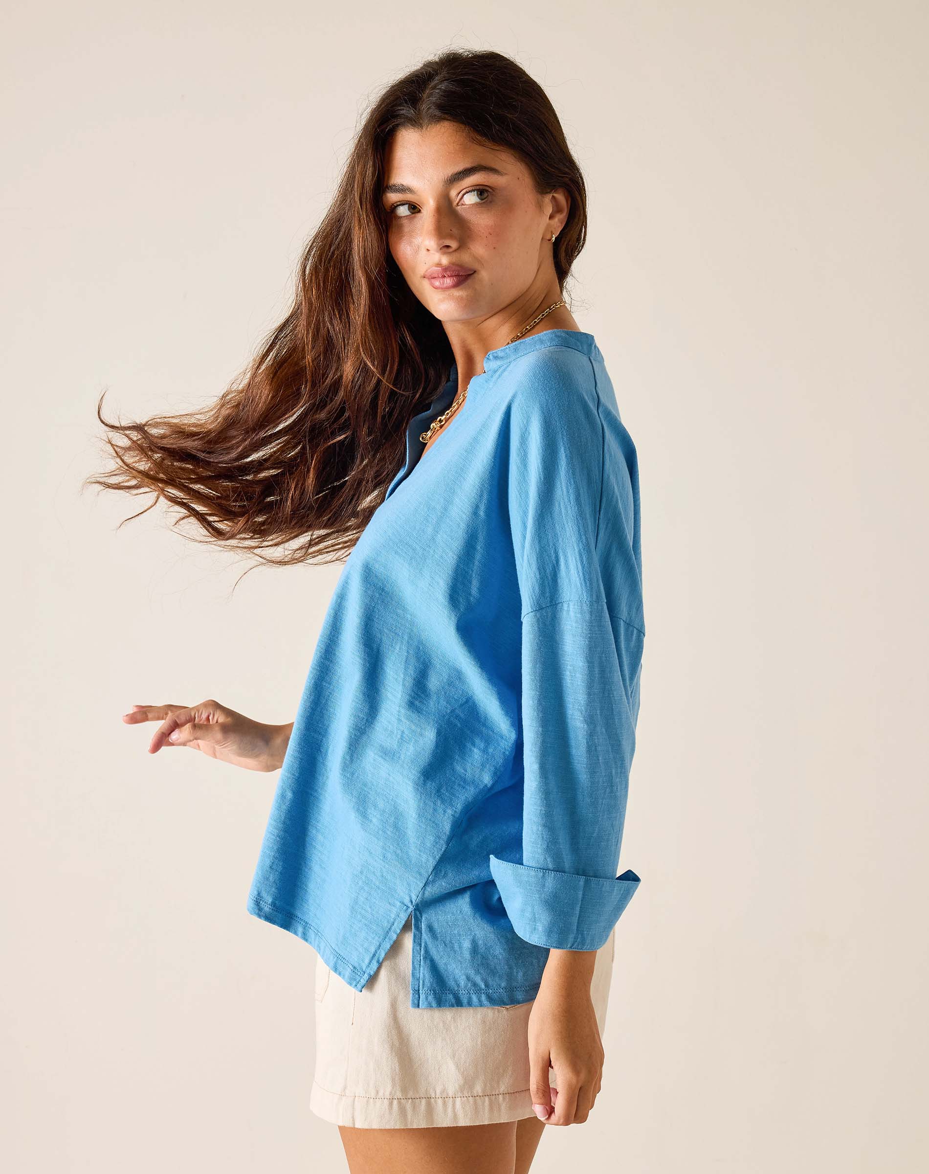 Woman wearing a blue shirt and white shorts against a plain background