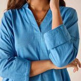 Woman wearing a blue shirt with rolled-up sleeves against a neutral background