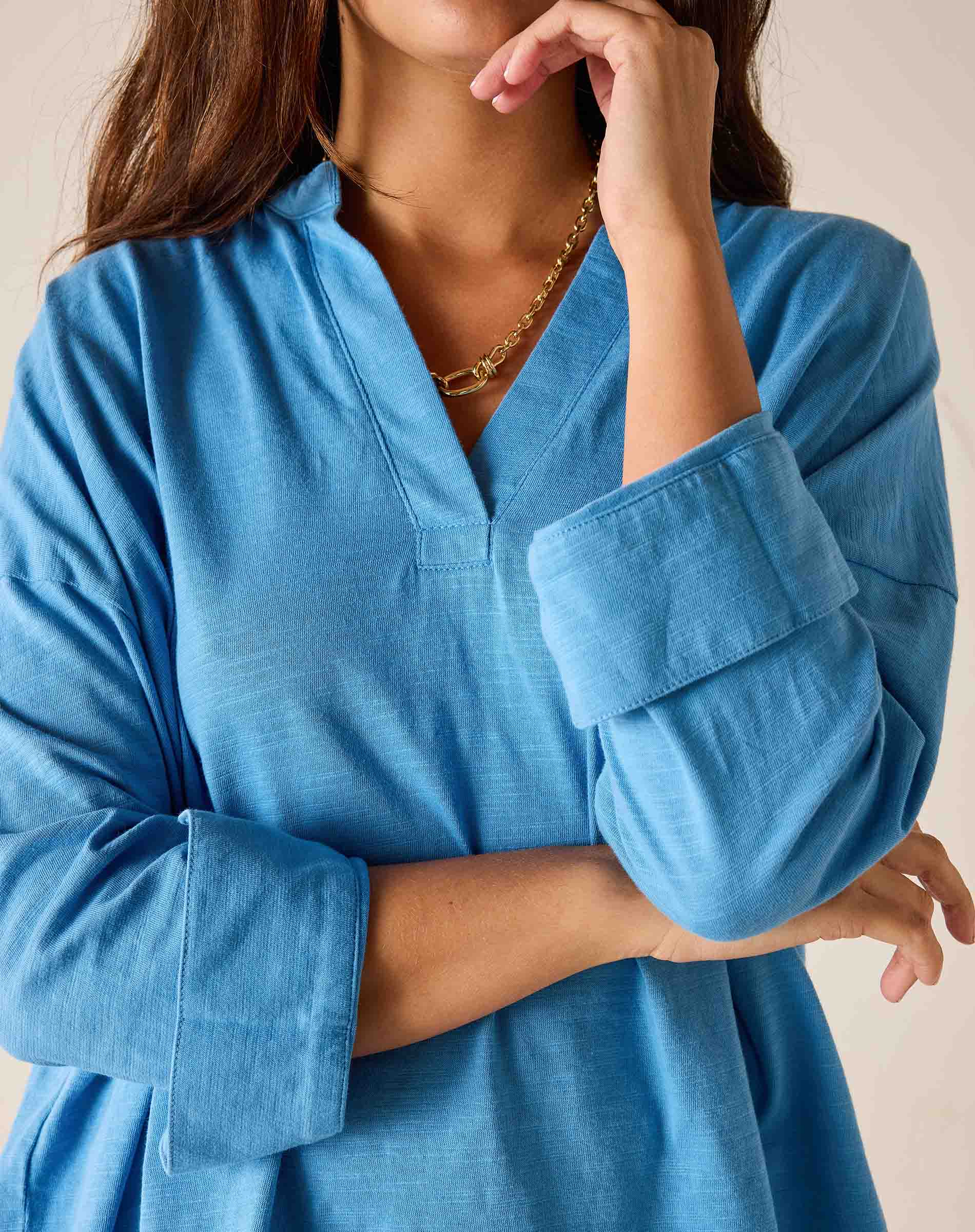 Woman wearing a blue shirt with rolled-up sleeves against a neutral background