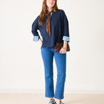 Woman wearing a navy shirt, blue jeans, and sneakers on a plain background