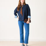 Woman wearing a navy shirt, blue jeans, and sneakers on a plain background