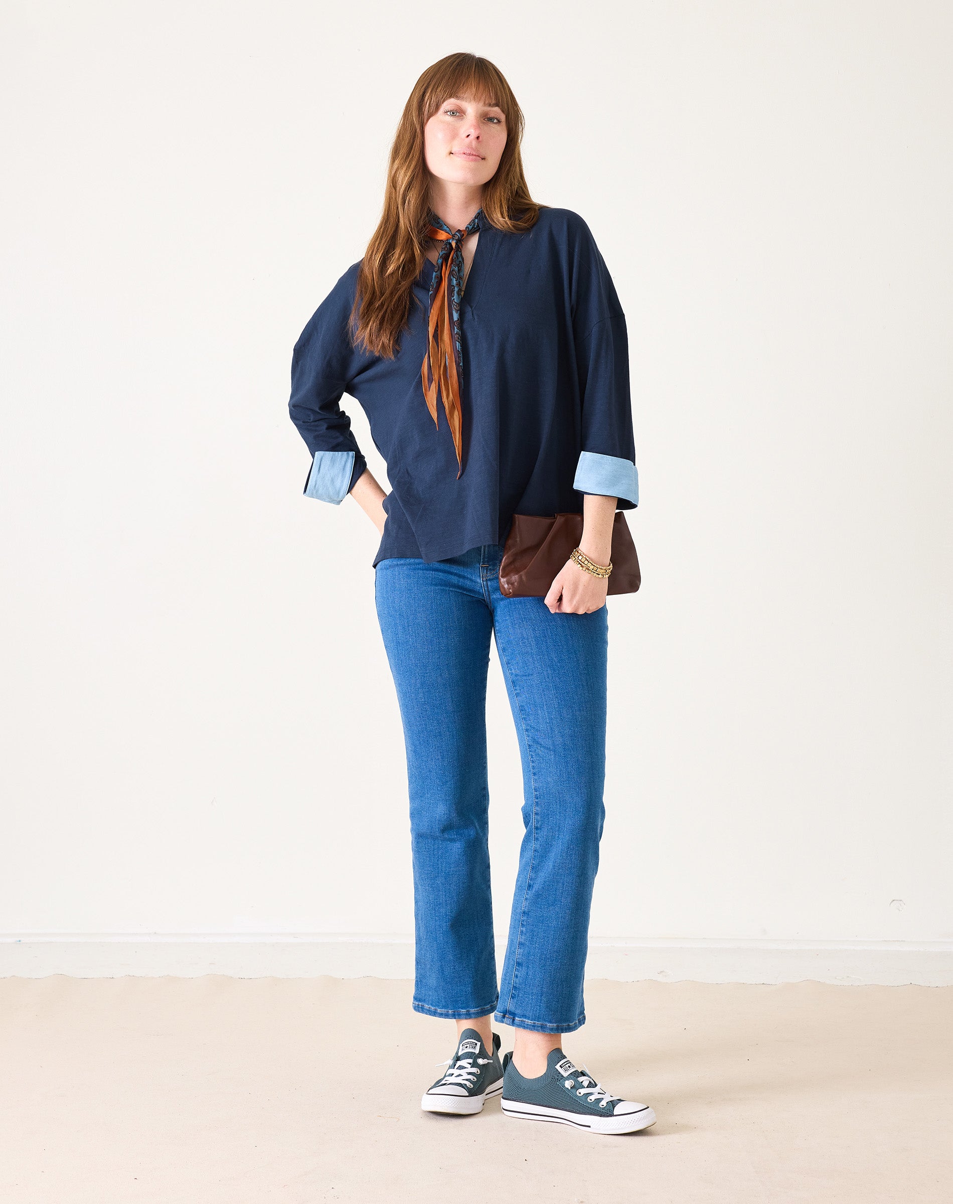 Woman wearing a navy shirt, blue jeans, and sneakers on a plain background