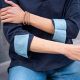 Person wearing a navy shirt with light blue cuffs and jeans, sitting on a stone surface.