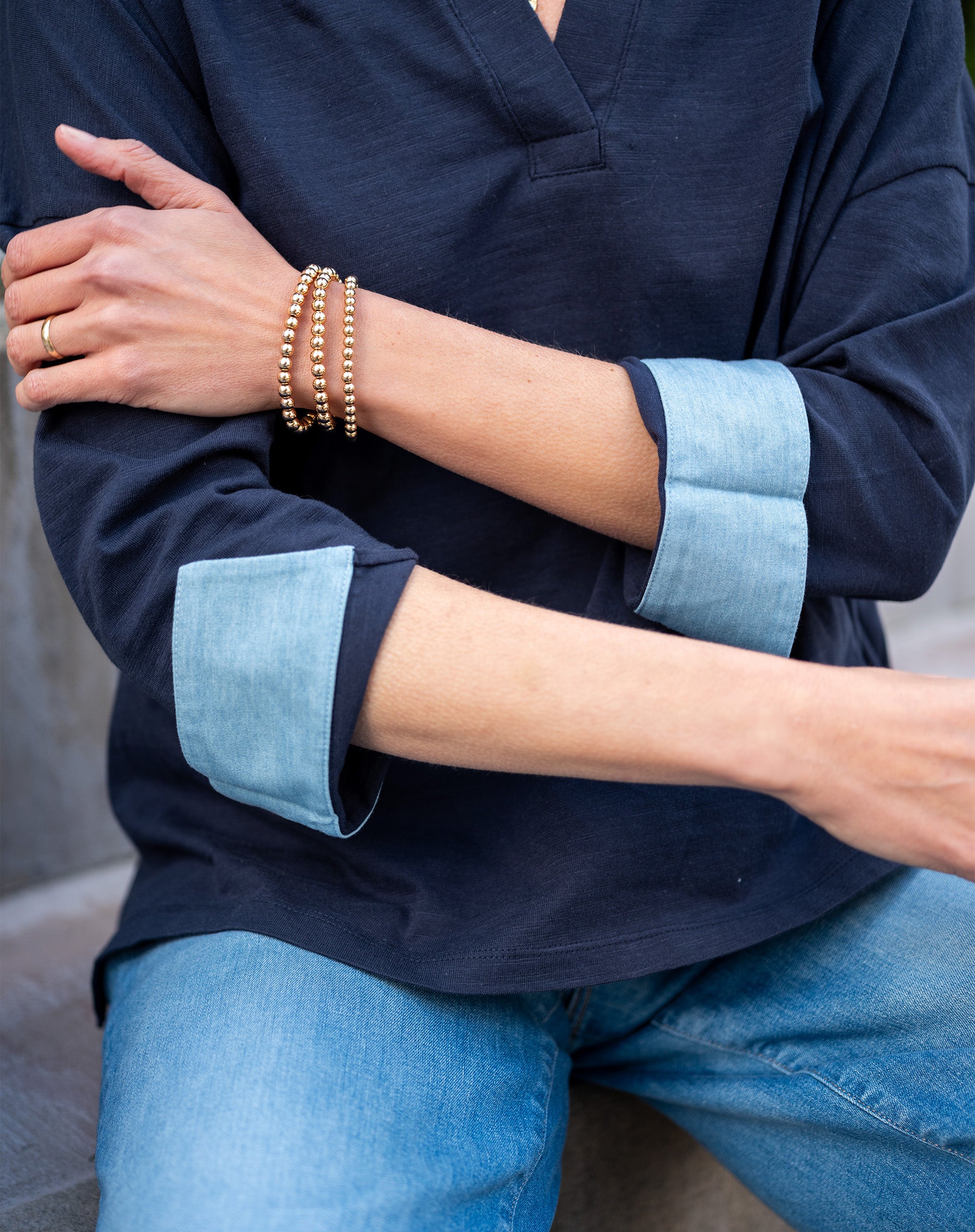 Person wearing a navy shirt with light blue cuffs and jeans, sitting on a stone surface.