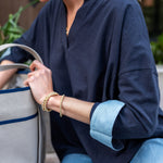 Person wearing a navy blue shirt with rolled-up sleeves, holding a gray bag.