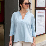 Woman wearing a light blue shirt and sunglasses standing outside a building.