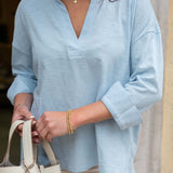 Person wearing a light blue shirt with rolled-up sleeves, holding a beige handbag.