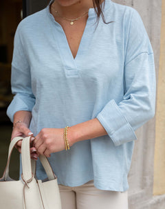 Person wearing a light blue shirt with rolled-up sleeves, holding a beige handbag.