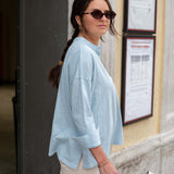 Woman wearing a light blue shirt and sunglasses, standing outdoors.