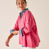 Woman wearing a pink shirt with denim sleeves against a beige background