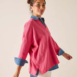 Woman wearing a pink shirt with blue cuffs and collar against a beige background