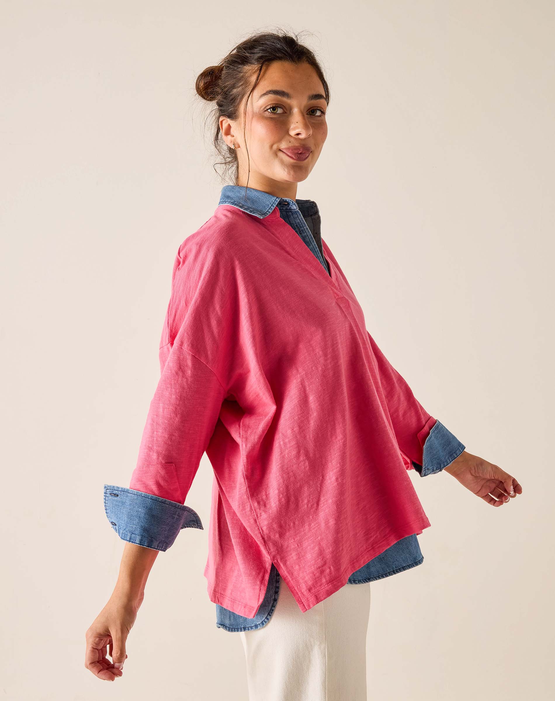Woman wearing a pink shirt with blue cuffs and collar against a beige background