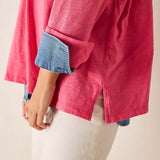Person wearing a pink shirt with rolled-up denim sleeves on a beige background