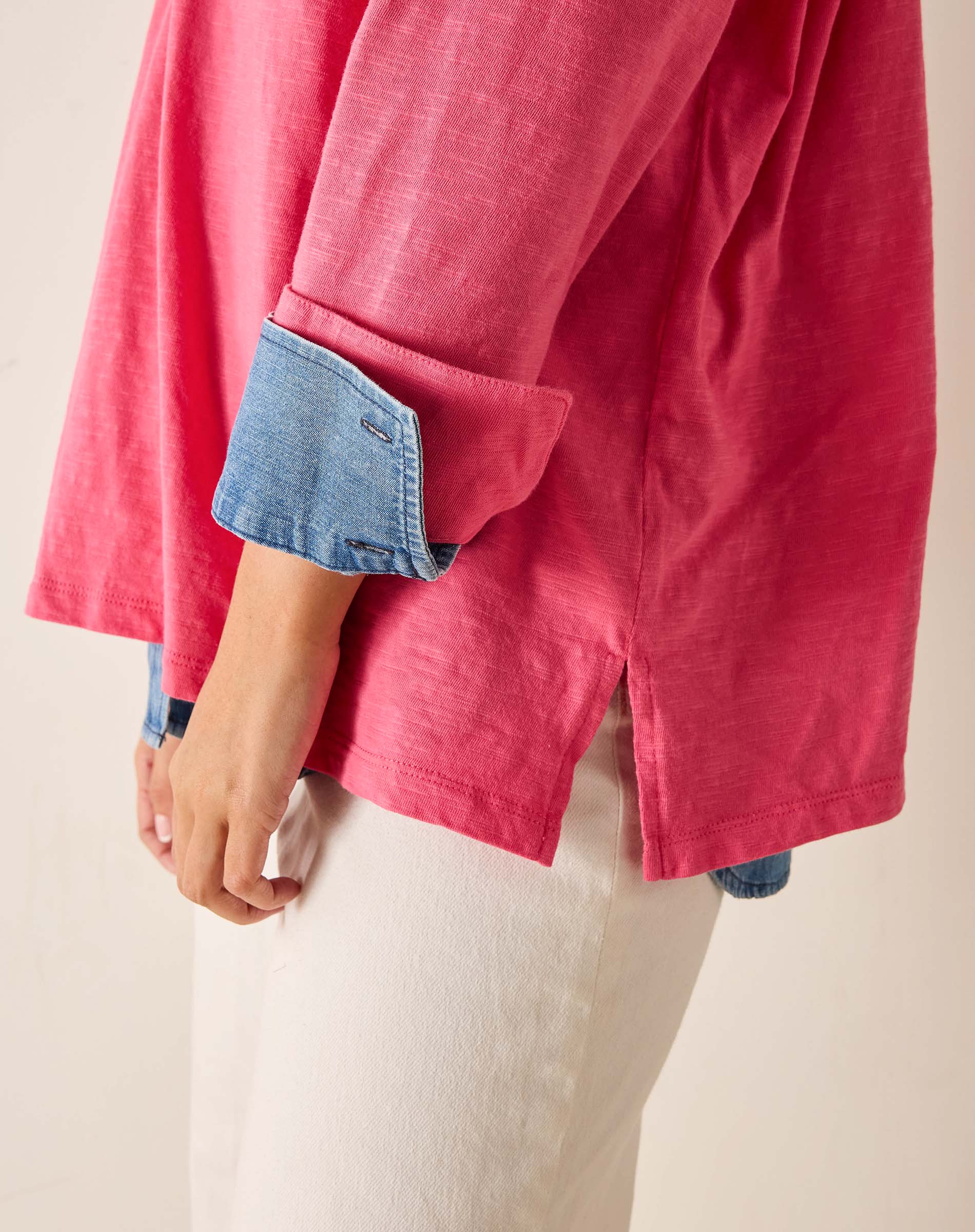 Person wearing a pink shirt with rolled-up denim sleeves on a beige background