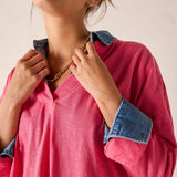 Person wearing a pink shirt with rolled-up denim sleeves, holding a gold chain necklace.