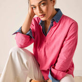 Woman wearing a pink shirt with rolled-up sleeves and white pants sitting on a chair.
