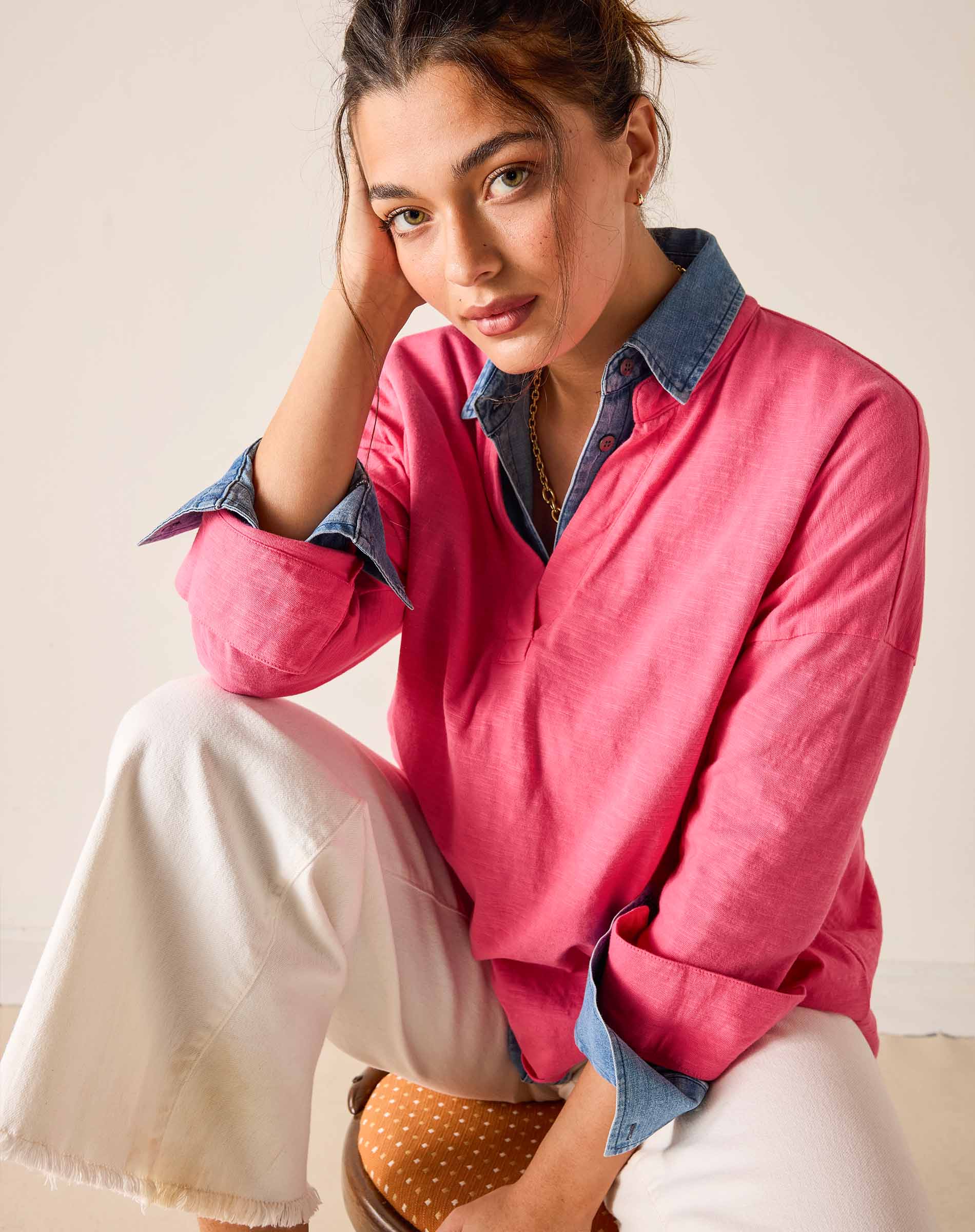Woman wearing a pink shirt with rolled-up sleeves and white pants sitting on a chair.