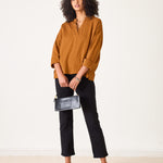 Woman wearing a mustard yellow blouse and black pants, holding a black clutch against a white background